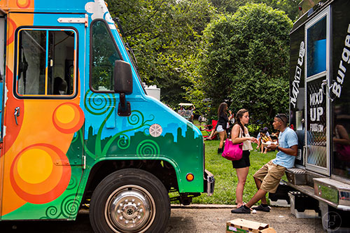 Melaniie Taylor (left) and Alex Zaciato sit in between food trucks as they eat during the Atlanta Street Food Festival at Piedmont Park in Atlanta on Saturday, July 11, 2015. 