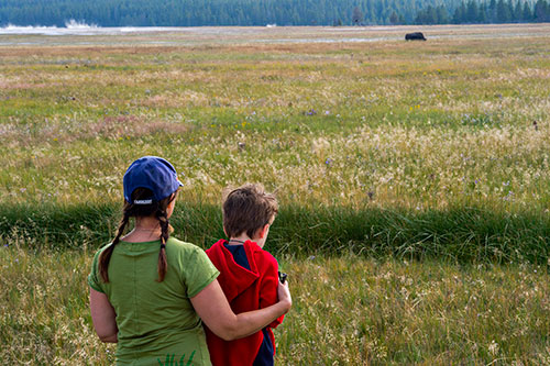 A woman hugs her son as they watch a bison graze near one of the many geysers inside Yellowstone National Park in Wyoming on Thursday, August 6, 2015.