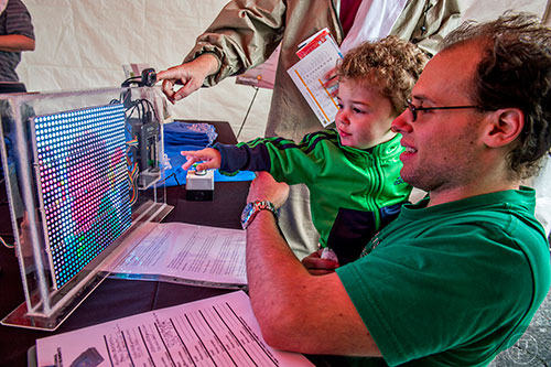 Leo DeAngelis (center) and his father Matt look at themselves projected on a LED display during the Atlanta Maker Faire in Decatur on Saturday, October 3, 2015. 