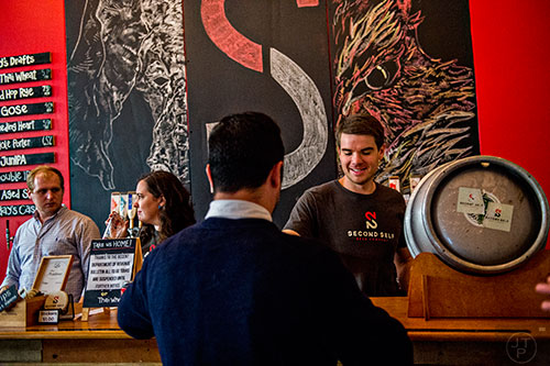 Harris Hornbuckle (right) hands a beer to Craig Hoover as he tends bar with Liz Hartnett and Alex Kaas during the Second Self Beer Company's one year anniversary celebration in Atlanta on Saturday, October 3, 2015. 