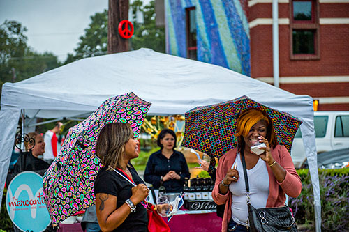 Billie Harris (left) and Dekeytra Walker protect themselves from the rain as they drink wine during the Kirkwood Wine Stroll on Friday.