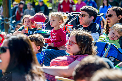 Mira Sonenblum (center) sits on her father Jason's lap as they listen to music during the Oakhurst Porch Fest on Sunday.