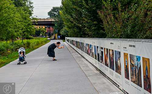 A woman leans in to take a photograph of Atlanta Celebrates Photography's piece for Art on the Beltline "The Fence at Photoville".