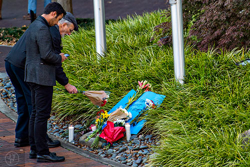 Bill Moon (left) adds a bouquet of flowers to a small memorial outside of the Consulate General of France's offices at the Buckhead Tower at Lenox Square in Atlanta on Saturday, November 14, 2015. Moon was one of around a dozen people that held a short vigil in front of the flags that lay at half staff.   