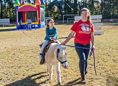 Lillian Troso (left) rides a pony guided by Miranda Miron during the Dunwoody United Methodist Church Holiday Festival on Saturday, November 14, 2015. 