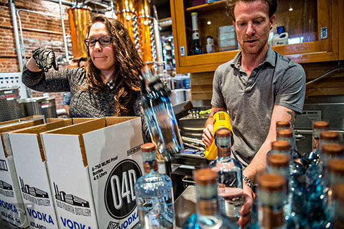 Jeff Moore uses a heat gun to seal bottles of vodka as Shannon Eggleton places them into boxes to be shipped during bottling day at Old Fourth Distillery in Atlanta.