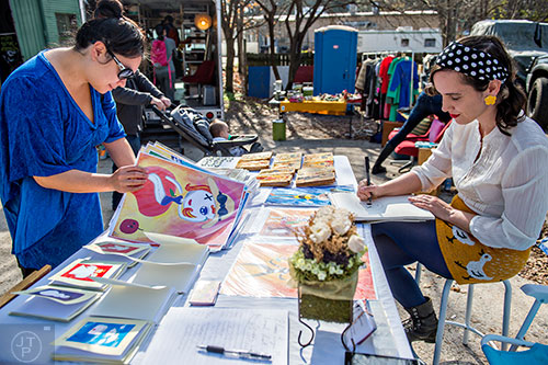 Jeanie Dizon (left) looks through Abby Schomaker's artwork while she draws a new piece during the Bazaar on the Beltline at The Hanger off of the Eastside Trail in Atlanta on Saturday, December 12, 2015. 
