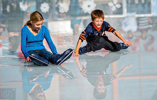Ashlyn Johnson (left) and Jack Andrews slide through the water collecting on the ice at the rink at Avalon in Alpharetta on Saturday, December 26, 2015. 
