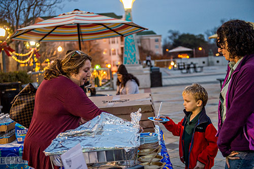 Carol Epstein (left) hands Andrew Sugarman and his mother Elysa a potato latke during the Chanukah celebration in Decatur Square on Thursday