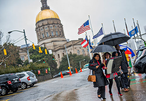 Cynthia Evers (left), Cori Ameen and Stephen Woodall use umbrellas to shield themselves from the rain as they walk to their cars after leaving the state capitol building in Atlanta on Friday, January 22, 2016. 