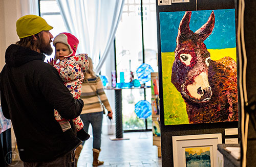 Ben James (left) holds his daughter Presley June as they look at a painting by Corey McNabb during the Callanwolde Arts Festival in Atlanta on Saturday, January 23, 2016. 