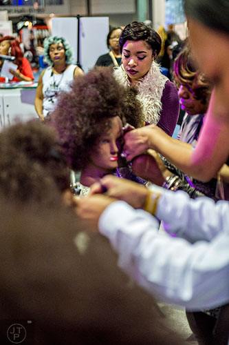Maquia Aniase (center) practices hair styling on a dummy during the Bronner Brothers International Beauty Show at the Georgia World Congress Center in Atlanta on Saturday, February 20, 2016.