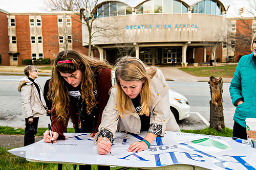Sarah Norman (left) and Sara Stubbs, the organizers of the Rally for Riley, write messages to Susan Riley on a sign as they set up for the event across from Decatur High School on Monday morning.