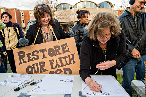 Mary Rigger (left) and Lynne Norman crowd around a table to write Susan Riley letters during the Rally for Riley across from Decatur High School on Monday morning.