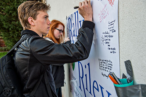 Matthew Tatum (left) and Iris Quam write messages for Susan Riley on a sign during the Rally for Riley across from Decatur High School on Monday morning.