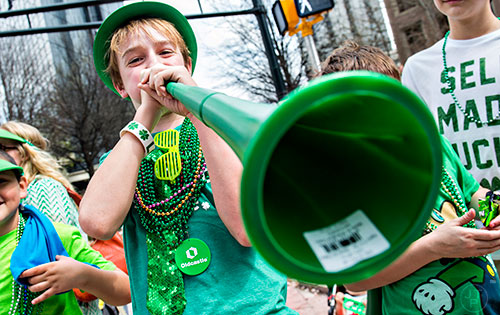 Jacob Zwiger (center) blows his horn as he watches the annual Atlanta St. Patrick's Day Parade pass by on Saturday, March 12, 2016. 