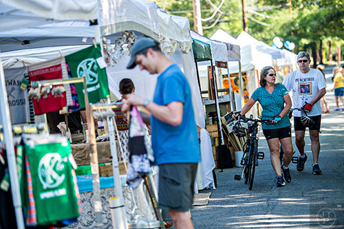 Carol Hostetter (center) and her husband Spencer walk their bikes past the artist booths during the Kirkwood Spring Fling on Saturday.