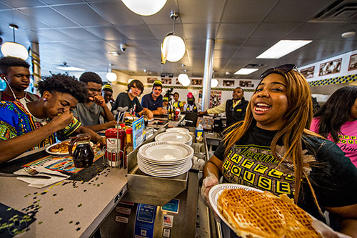 Micaiah Leslie (right) is ready to replenish contestants with a plate of fresh waffles during the waffle eating contest at the Waffle House off of Decatur Square on Friday.