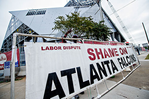 People stand outside the construction zone of Mercedes Benz Stadium in Atlanta off of Northside Dr holding a labor dispute sign.